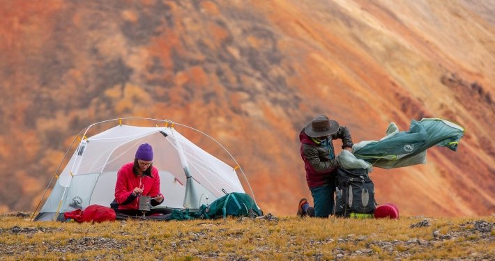 man packs up a small 2 person tent in front of a mountain backdrop