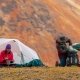 man packs up a small 2 person tent in front of a mountain backdrop