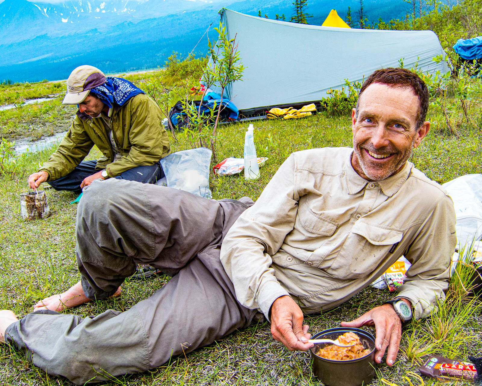 a hiker smiles as he eats backpacking food in Alaksa