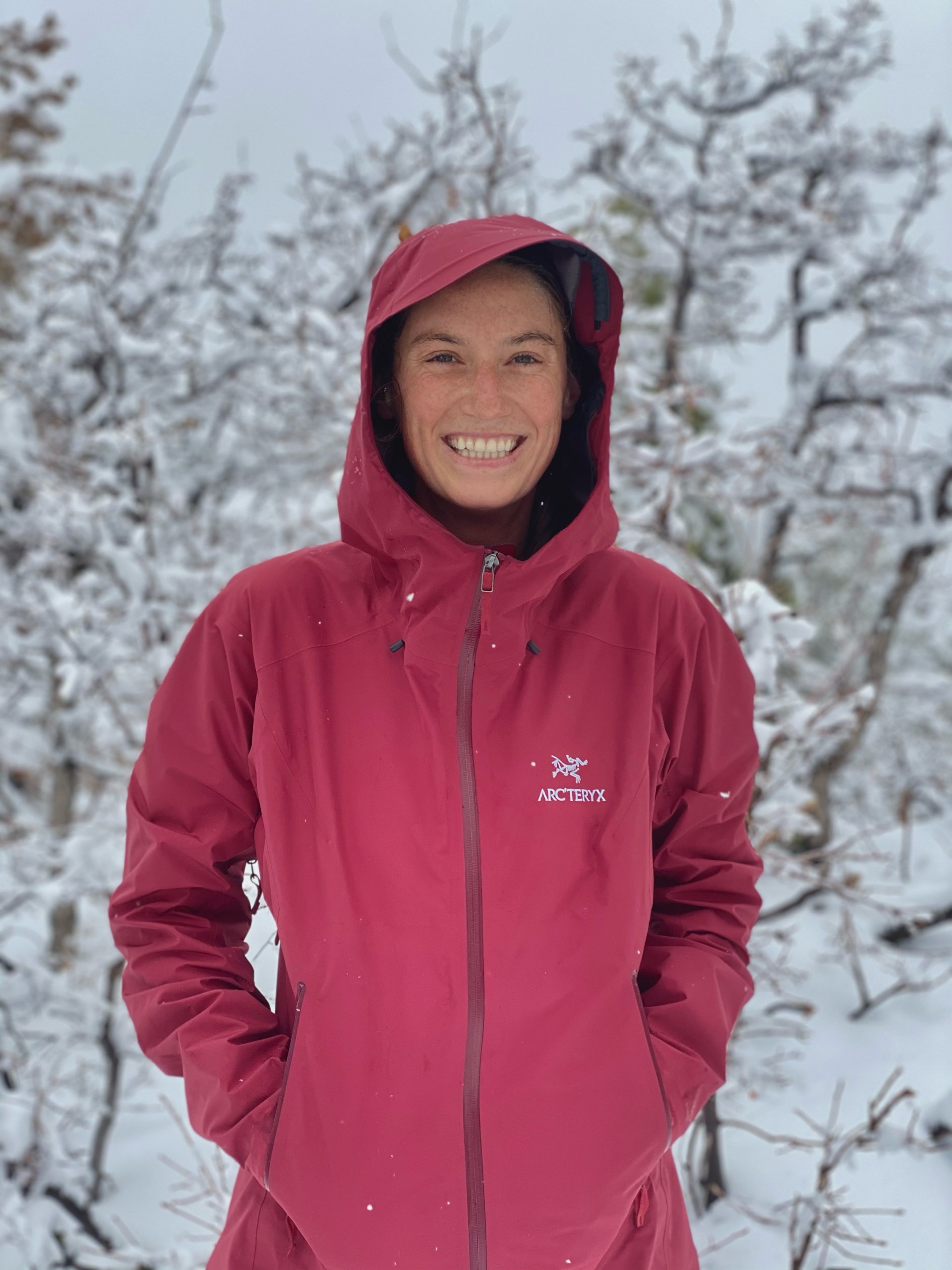 hiker in the snow smiling wearing a red arcteryx beta lt jacket