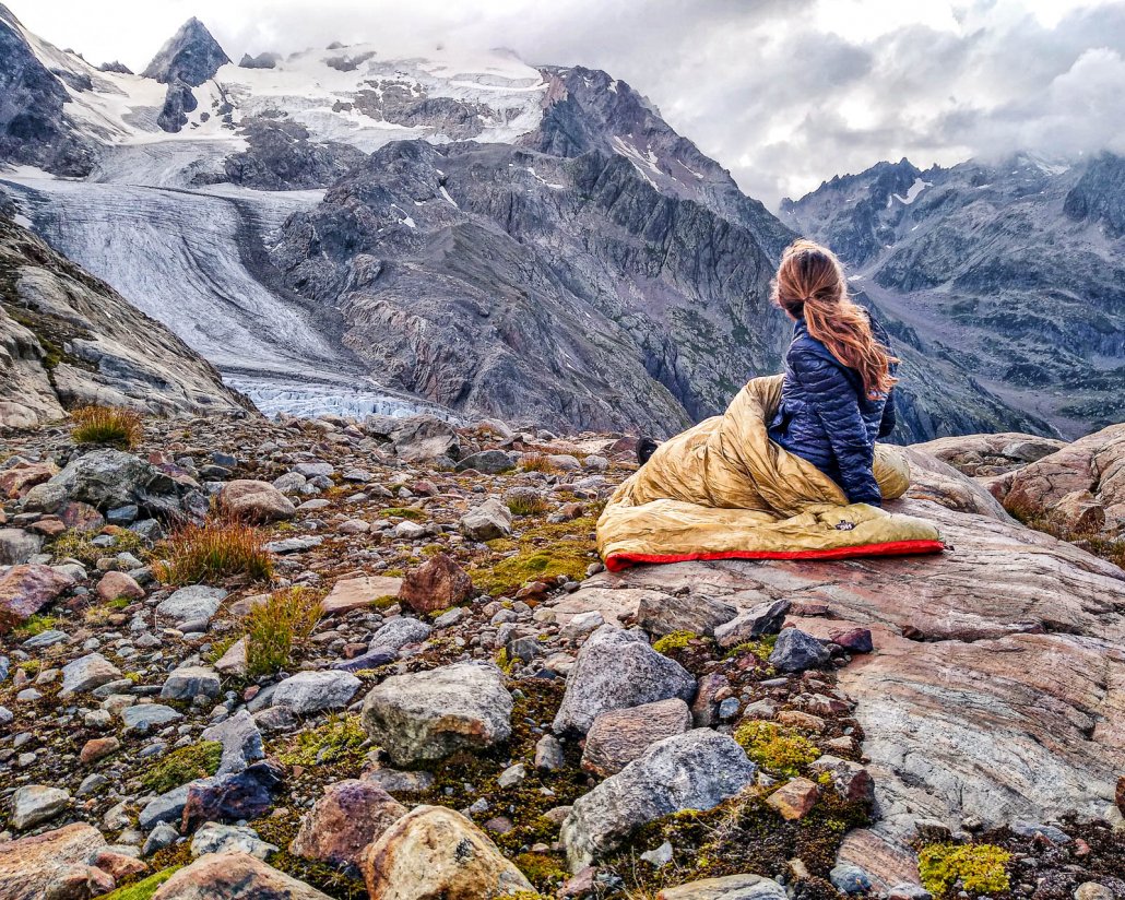 a woman gazes onto a glacier while testing the best backpacking quilts and sleeping bags