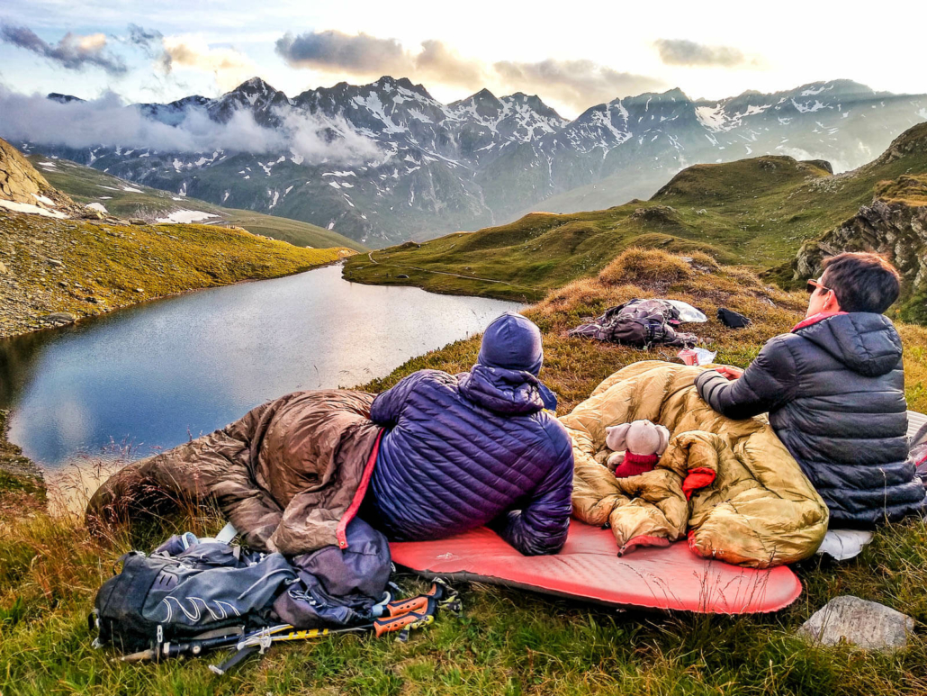 a couple relaxes in cozily in their backpacking quilts above a lake