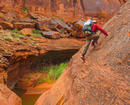 a man in hiking pants climbs through desert sandstone