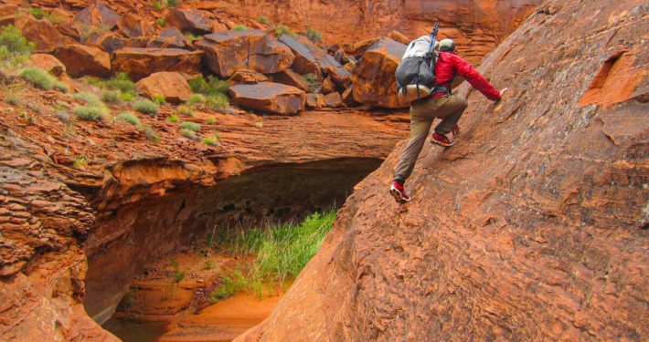 a man in hiking pants climbs through desert sandstone