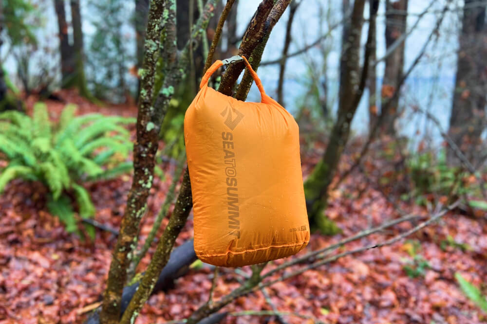 a backpacking dry bag hangs from a tree